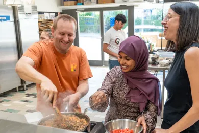Drei Personen stehen lachend am Herd