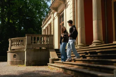 Zwei Teilnehmende von Meet'nSpeak gehen gemeinsam eine Treppe vor einem Gebäude hinunter.