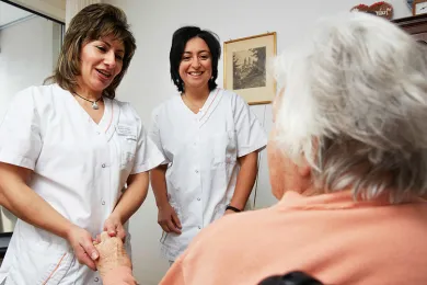 Zwei Pflegehelfende sprechen mit einer Bewohnenden in einem Alterszentrum.