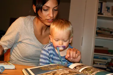 Eine Nanny schaut mit einem Kind ein Bilderbuch an. 