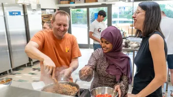 Drei Personen stehen lachend am Herd