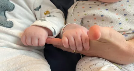 Eine erwachsene Hand hält die Hände von Zwillingsbabys