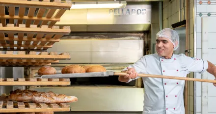 Hassan nimmt ein vorbereitetes Brot vom Blech, um es in den Holzofen zu schieben.