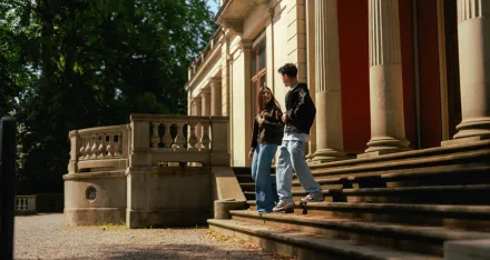 Zwei Teilnehmende von Meet'nSpeak gehen gemeinsam eine Treppe vor einem Gebäude hinunter.