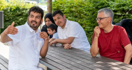 Eine geflüchtete Familie mit Kindern und ein Freiwilliger des Zürcher Roten Kreuzes sitzen in einem Park.