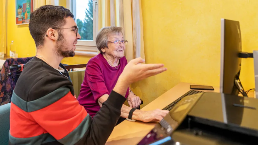 Ein Freiwilliger vom Jugendrotkreuz erklärt einer Bewohnerin etwas am Computer