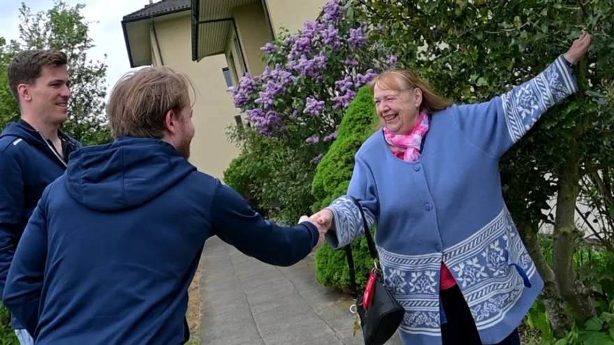 Eine Frau, die Fahrgast ist beim Zürcher Rotkreuz-Fahrdienst, wird von zwei prominenten Spielern des EHC Kloten begrüsst.