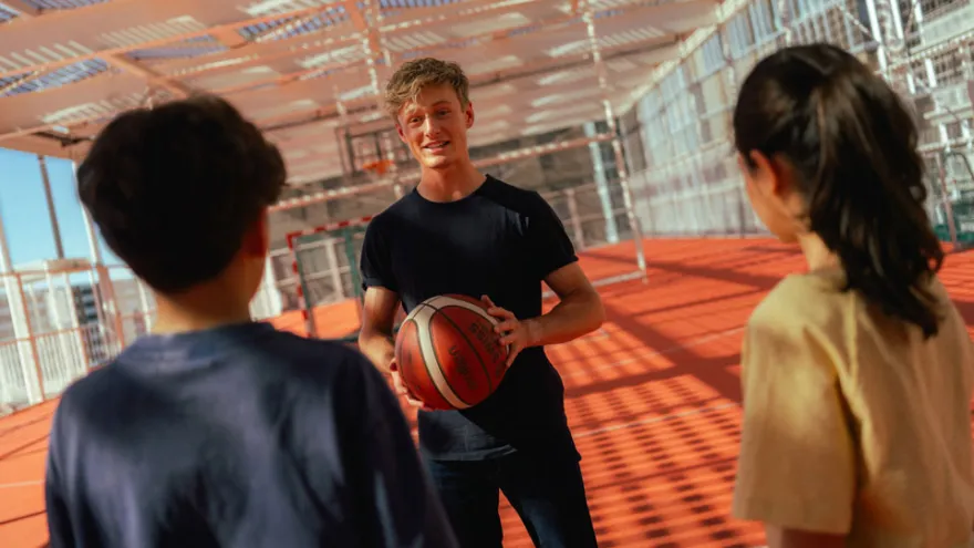 Ein Freiwilliger und zwei Kinder der Ferienwoche spielen gemeinsam Basketball.